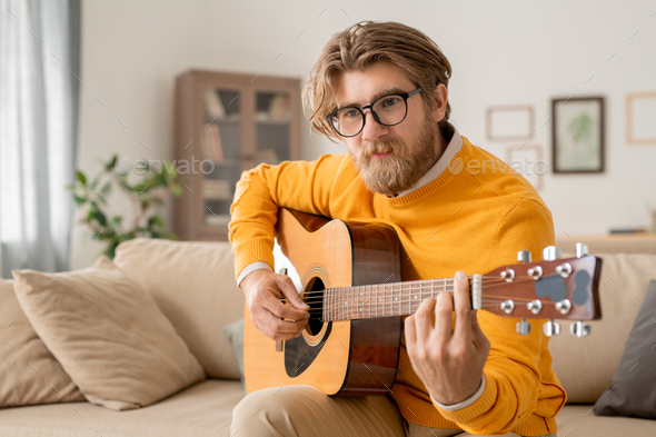 Young contemporary male musician in casualwear playing acoustic guitar