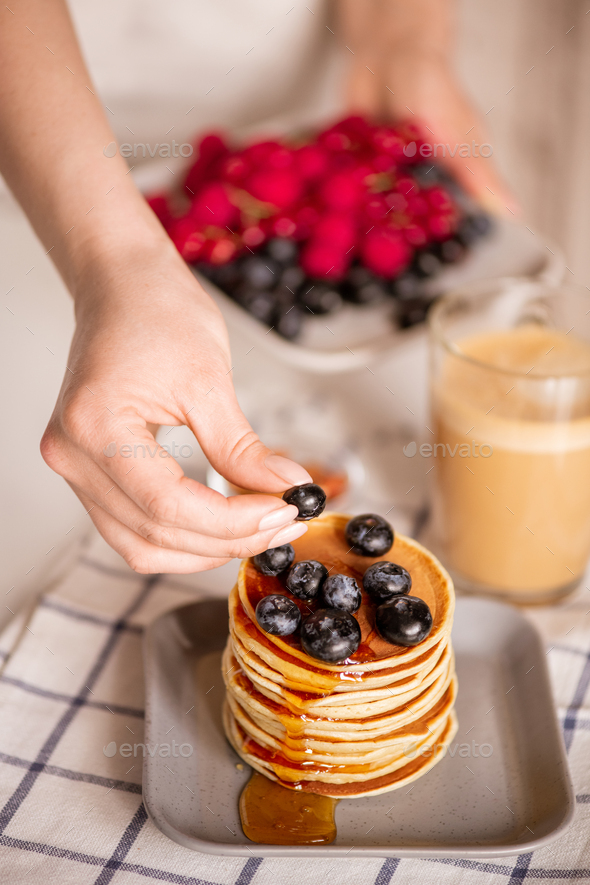 Hand of young woman putting fresh blackberry on top of appetizing crepe stack