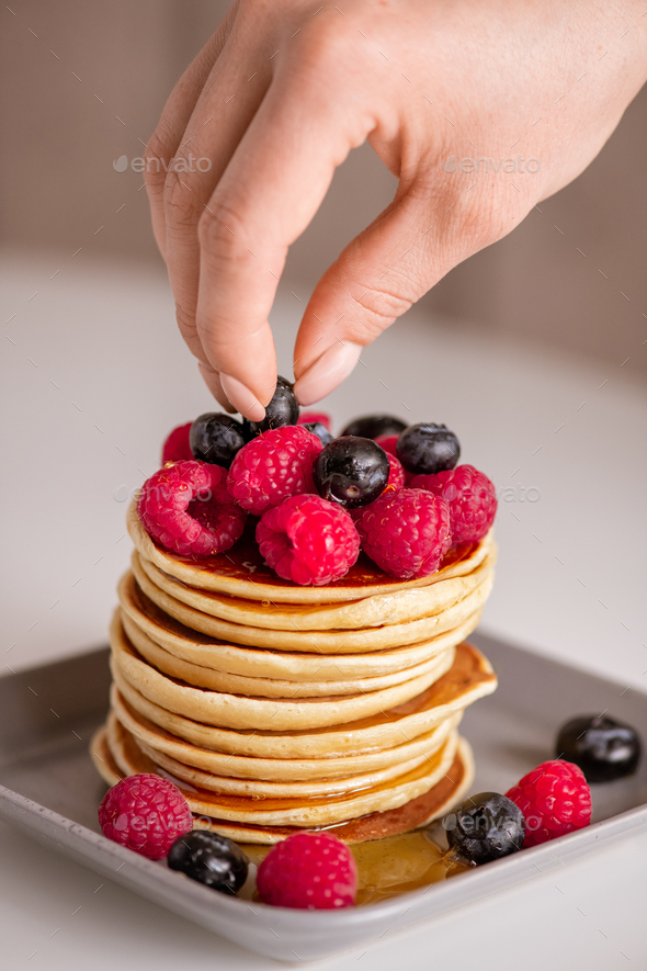 Hand of woman putting fresh raspberries and blackberries on top of crepe stack