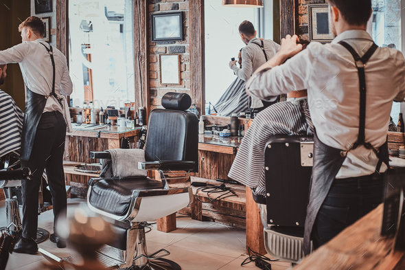 Thendy hairdresser at modern barbershop is working on client\'s haircut.