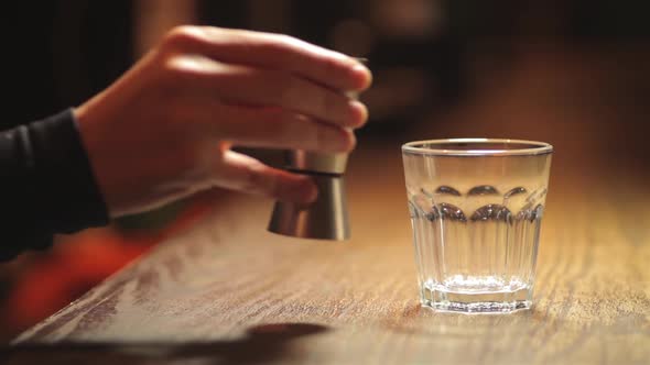 Hand pouring some whiskey in a glass, on a bar counter