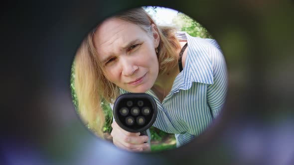 Woman Plugging in an Electric Car at Outlet Socket alt