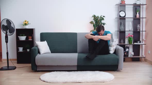 Unhappy depressed Caucasian man sits on sofa in living room feeling despair lonely suffering 