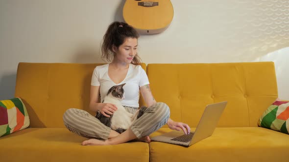 Young Asian Woman Surfing in Internet with Her Cat at Home on Coach alt