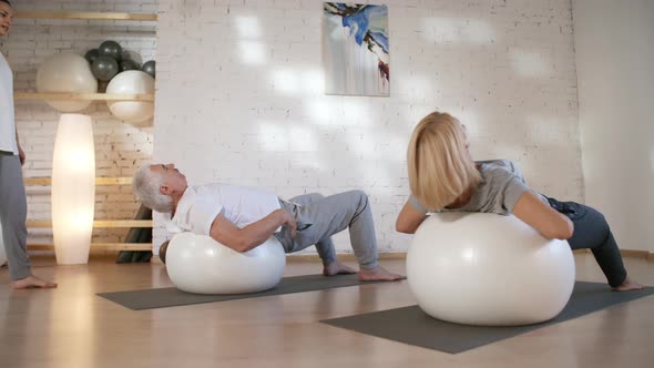 Caucasian Man and Woman Stretching on Stability Balls in Gym alt