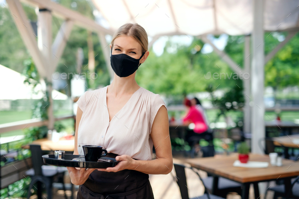Waitress with face mask serving customers outdoors on terrace restaurant