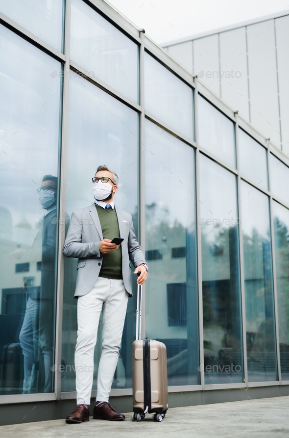 Businessman with luggage going on business trip, wearing face mask at the airport