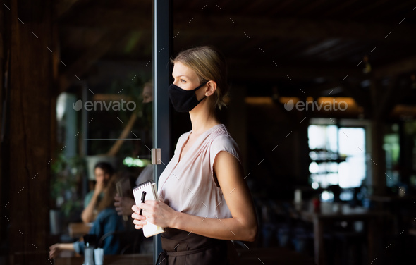 Side view of waitress with face mask standing at the door in restaurant