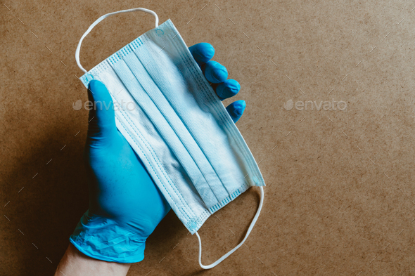 Hand in blue rubber gloves holds a medical mask.