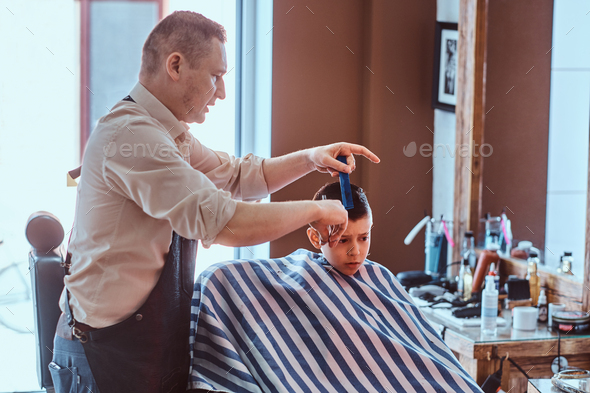 Small school boy had his first trendy haircut at modern barbershop.