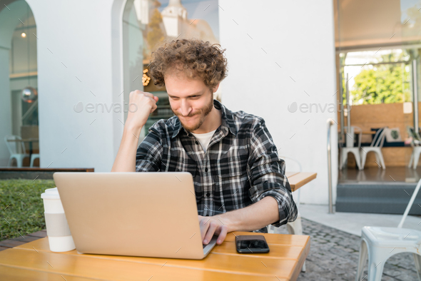 Happy man looking at laptop and celebrating good news.