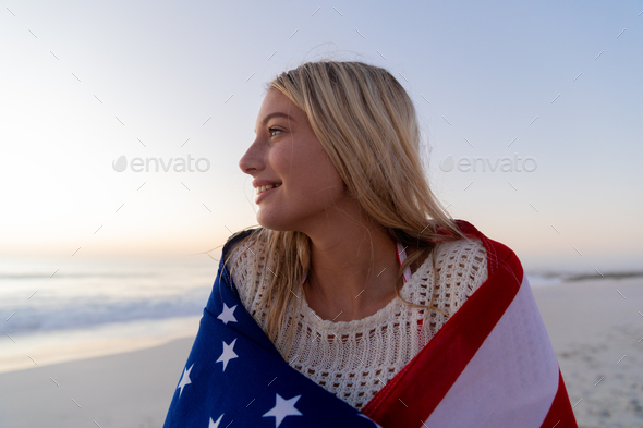 Caucasian woman covering herself with a US flag at the beach