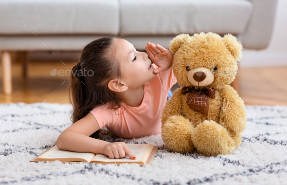 Little Asian Girl Whispering Sharing Secret With Teddy Bear Indoors