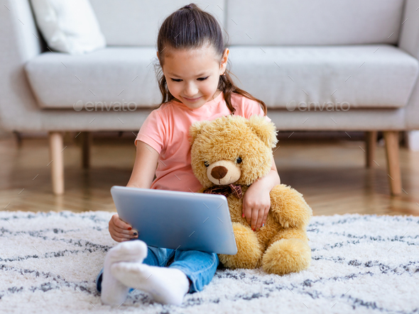 Girl Watching Cartoons On Tablet Hugging Teddy Bear At Home