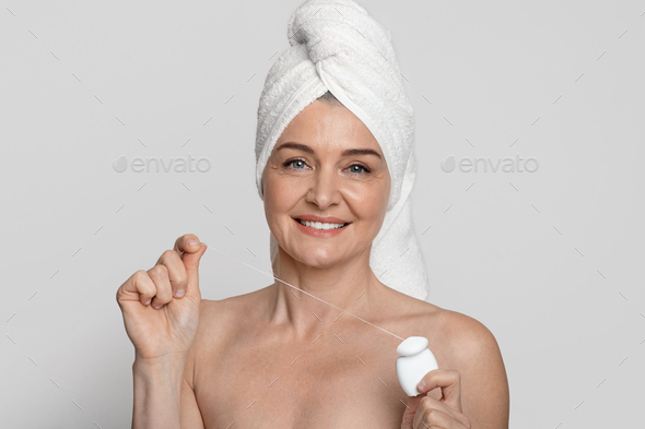 Tooth Care. Nude mature woman with towel on head holding dental floss