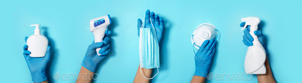 Raised hands in medical gloves holding masks, sanitizers, soap, non contact thermometer on blue