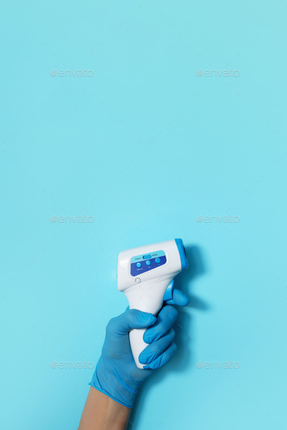 Hand in medical glove with digital infrared non contact thermometer gun for measuring temperature on