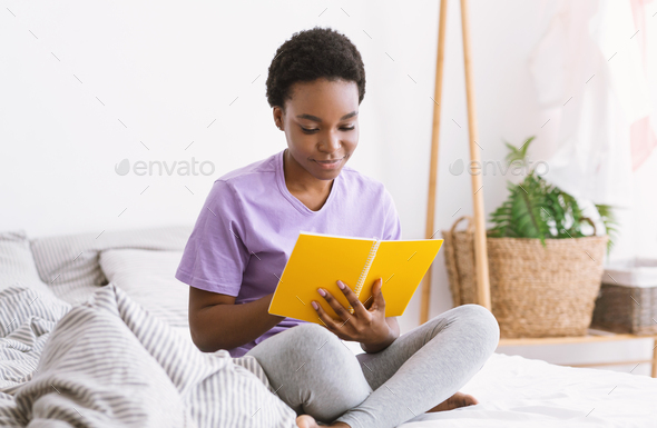 Work with notes. Woman reading notepad, sitting on bed in bedroom interior