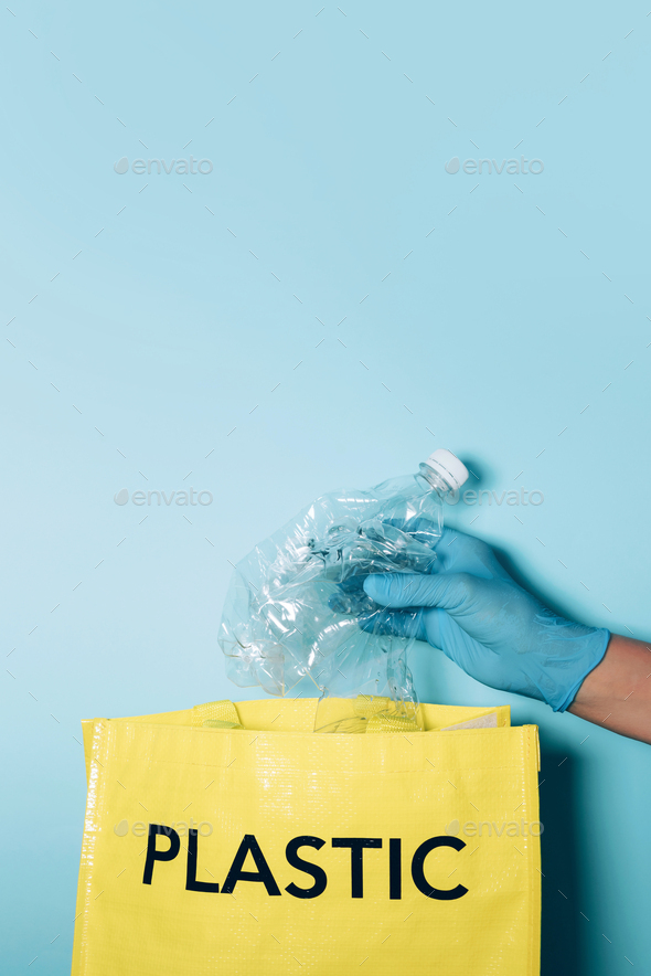 Hand in blue gloves puts plastic bottle in recycling bin. Environment care, sorting waste. Copy - Stock Photo - Images