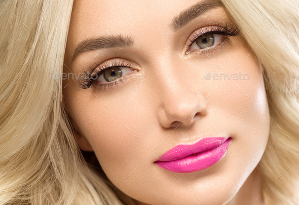 Beautiful blonde woman with lashes extension pink lips long curly hair face closeup gray background.