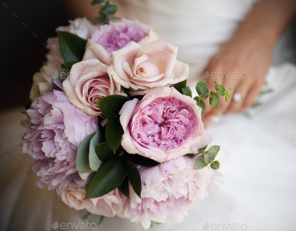 A woman, a bride holding a bridal bouquet of pastel coloured pale pink roses and lavender peonies.