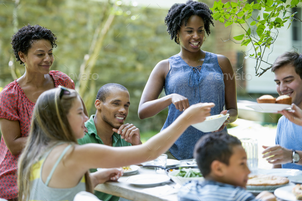 A family gathering, men women and children around a table in a garden in summer.