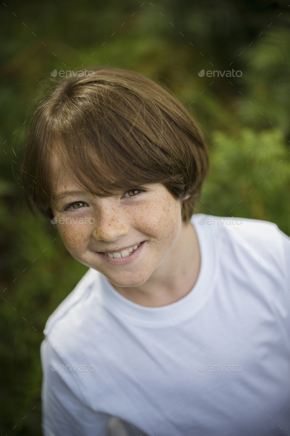 A boy in a white tee-shirt looking up at the camera.