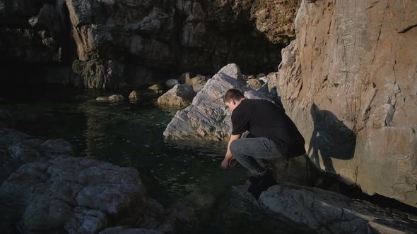 Young man in a black T-shirt is resting in a tent on the rocks by the sea alt