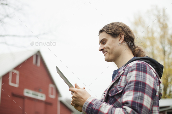 A young man using a computer tablet, a portable PC tablet device, on an organic farm.