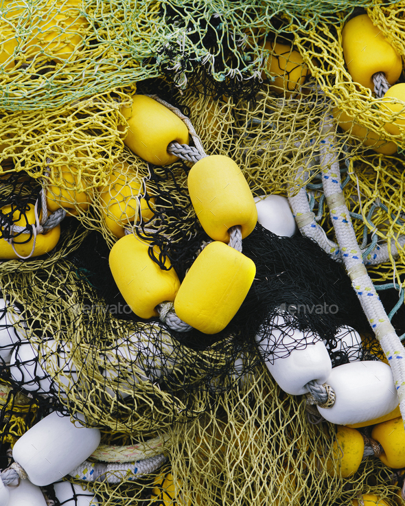 Pile of commercial fishing nets, with yellow and white floats, on the quayside