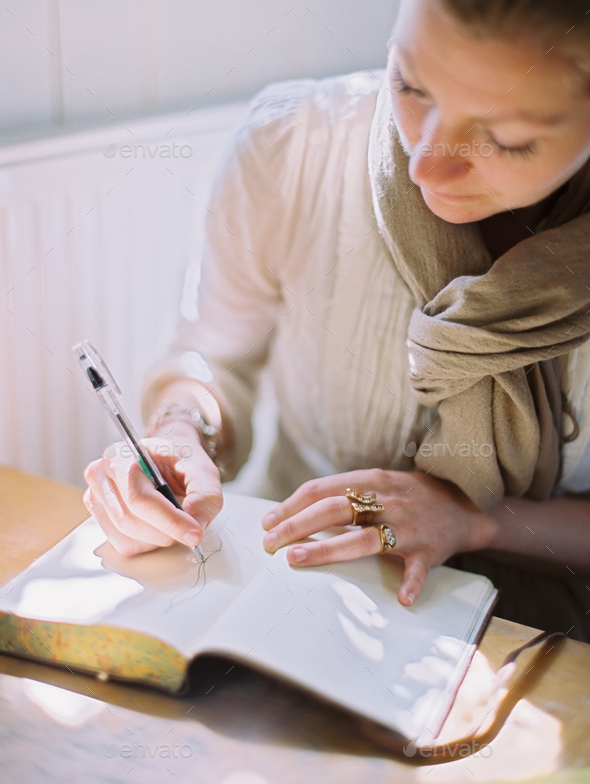 A woman using a coloured pen drawing on a blank page of a diary.