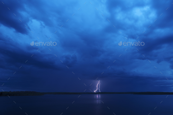 A lightning strike reflected in the water of a lake. Dark stormy dramatic sky.