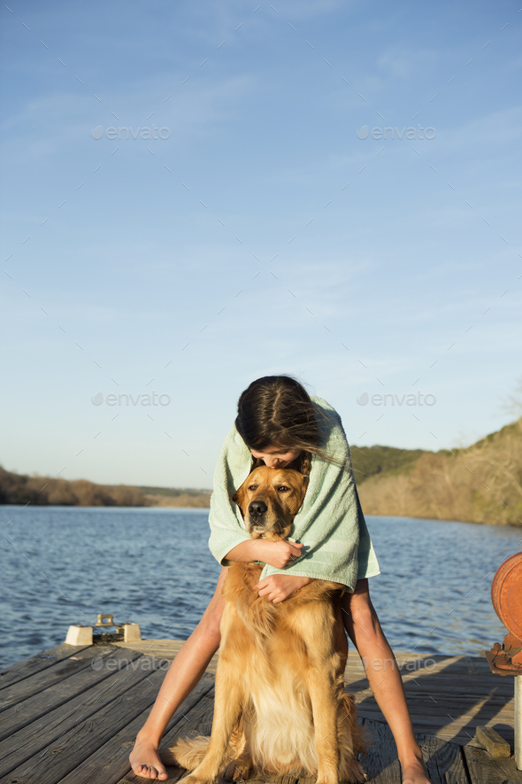 A girl in a swimming towel, cuddling a golden retriever dog.