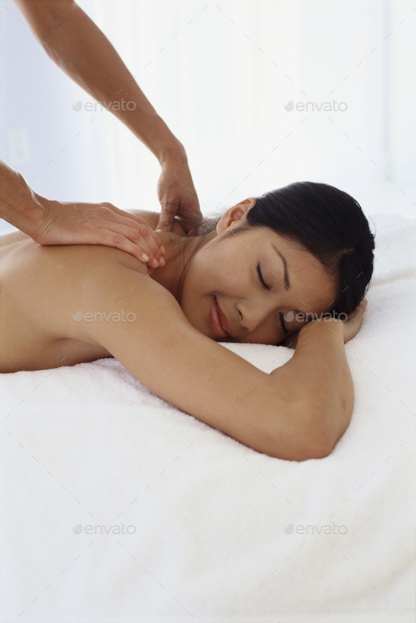 A young woman lying on her front having her shoulders massaged.