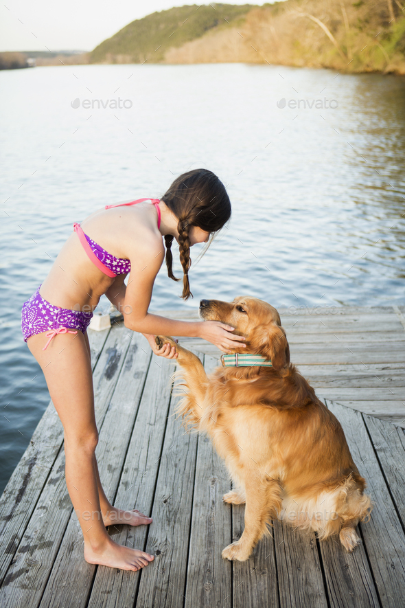 A girl in a bikini with a golden retriever dog lifting its paw up.