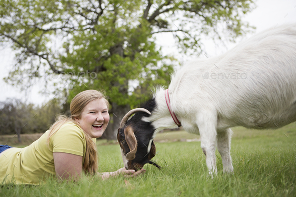A girl lying on grass head to head with a goat.