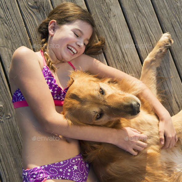 A girl in a bikini lying beside a golden retriever dog viewed from above