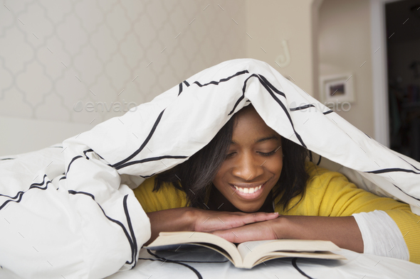 A young girl in her bed, under a duvet reading a book. - Stock Photo - Images