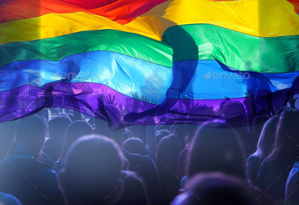 Colorful LGBT flag blows in the breez over crowd. - Stock Photo - Images