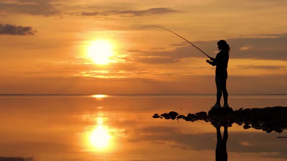 Woman Fishing on Fishing Rod Spinning at Sunset Background alt