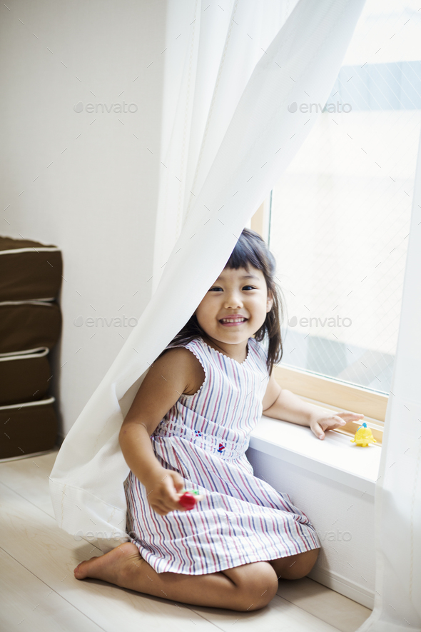 Family home. A girl playing by a window, hiding behind the net curtain. - Stock Photo - Images