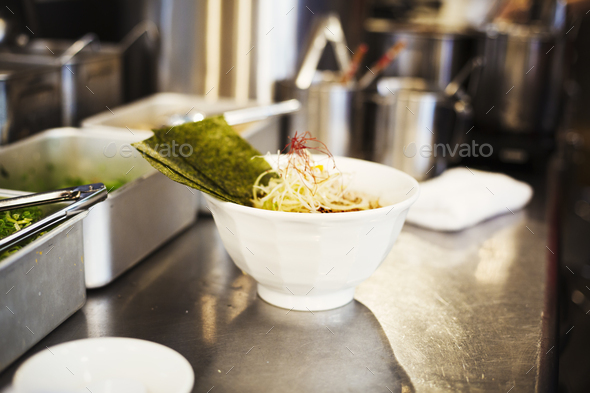 A ramen noodle shop kitchen. A chef preparing bowls of ramen noodles in broth, a speciality and fast food dish.