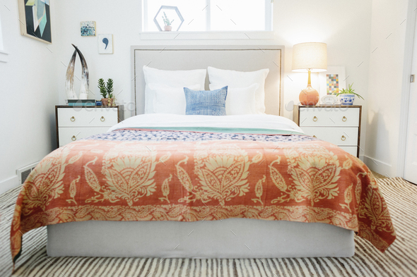 A bedroom in an apartment with a double bed and beside cabinets, and a vivid patterned bedspread.