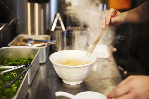 A ramen noodle shop kitchen. A chef preparing bowls of ramen noodles in broth, a speciality and fast food dish.