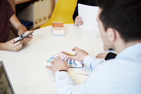 Three people round a table, one using a tablet, one showing a colour chart. Designers. - Stock Photo - Images