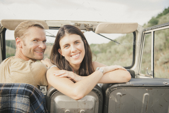 A couple on a road trip in a jeep side by side, a woman looking over her shoulder.