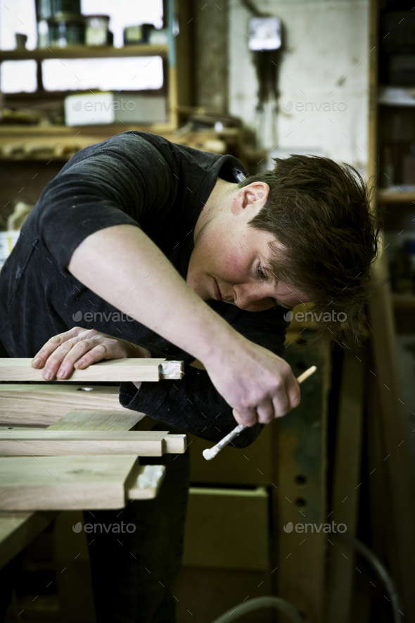 A woman working in a furniture maker\'s workshop using a small brush to apply glue to the wood.
