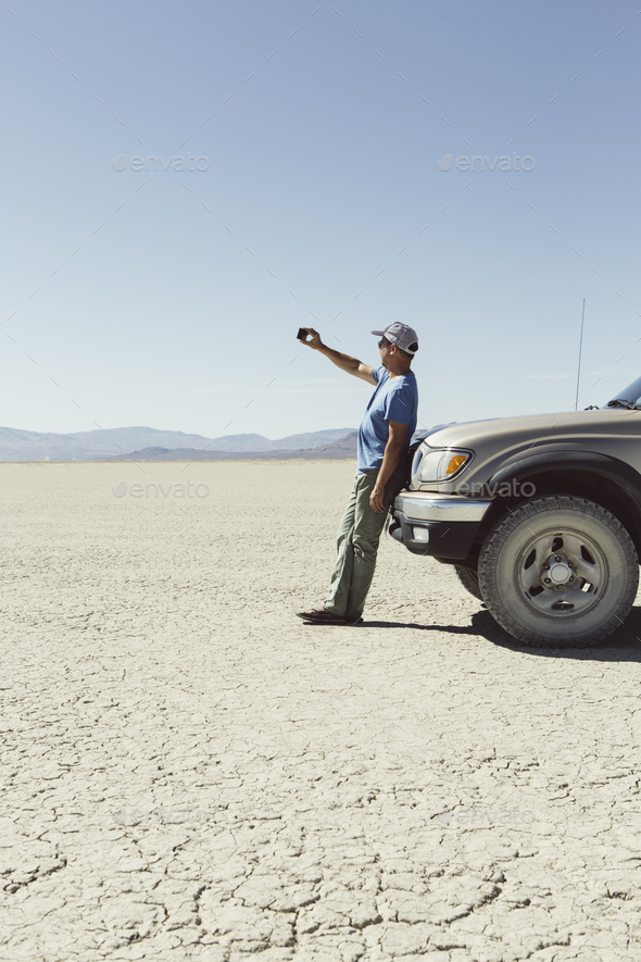 Man leaving against truck in desert, using smart phone, Black Rock Desert, Nevada