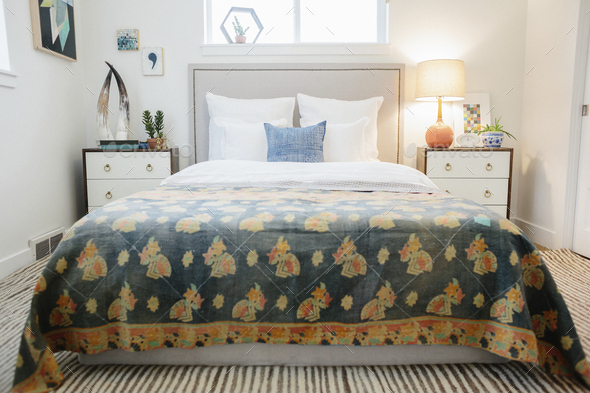 A bedroom in an apartment with a double bed and beside cabinets, and a vivid patterned retro look bed cover.