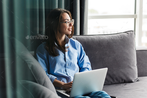 Image of woman working with laptop and smiling while sitting on couch